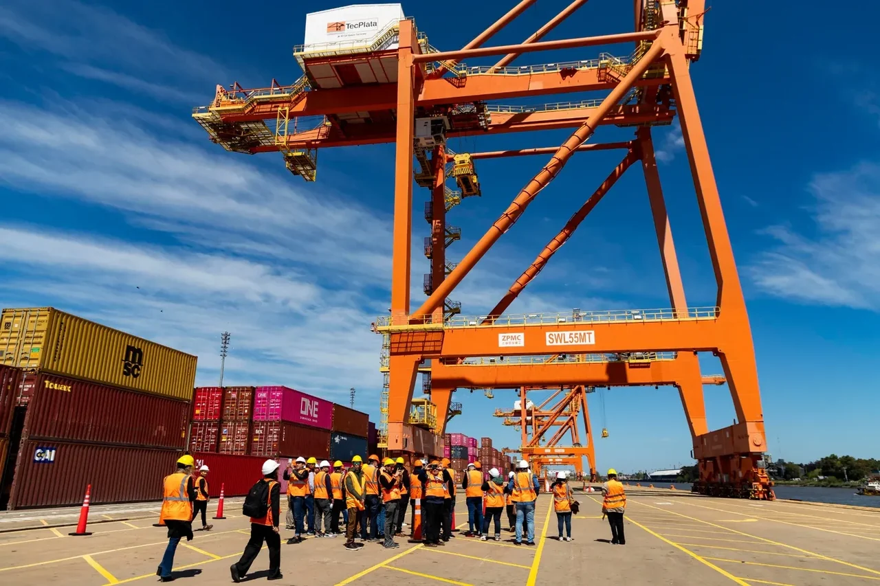 Grúa pórtico de una terminal de contenedores del Paraná con un grupo de visitantes de casco y chaleco durante una recorrida técnica